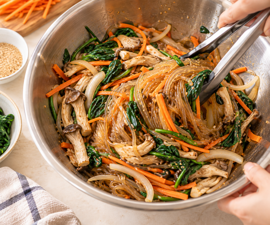 Glass noodles, mushrooms, and vegetables being tossed together in a large bowl